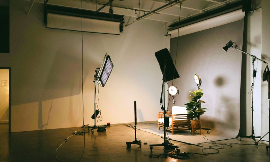 Estudio de fotografía con luces, fondo blanco y un sillón listo para una sesión