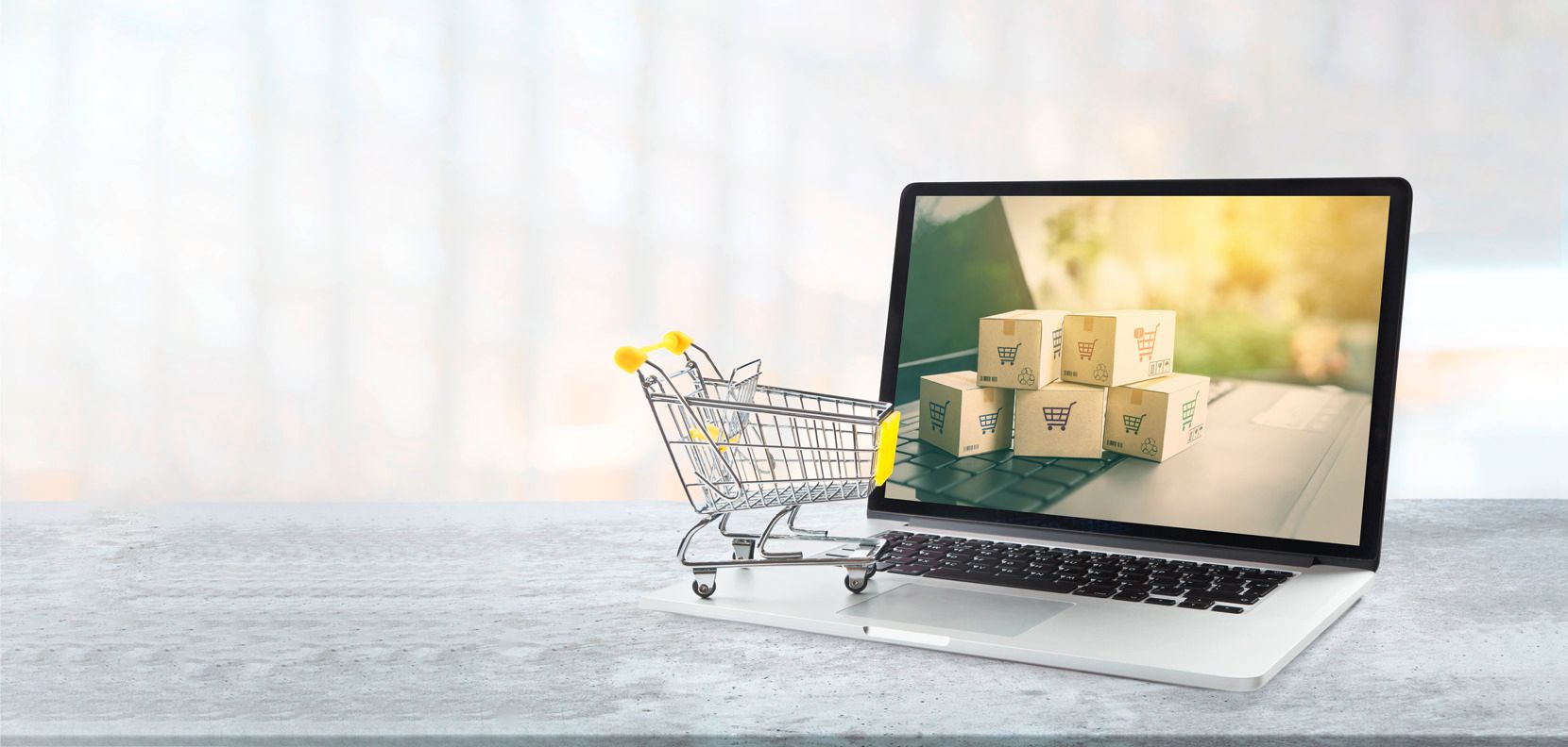 Carrito de compras en miniatura junto a una laptop que muestra cajas de envío